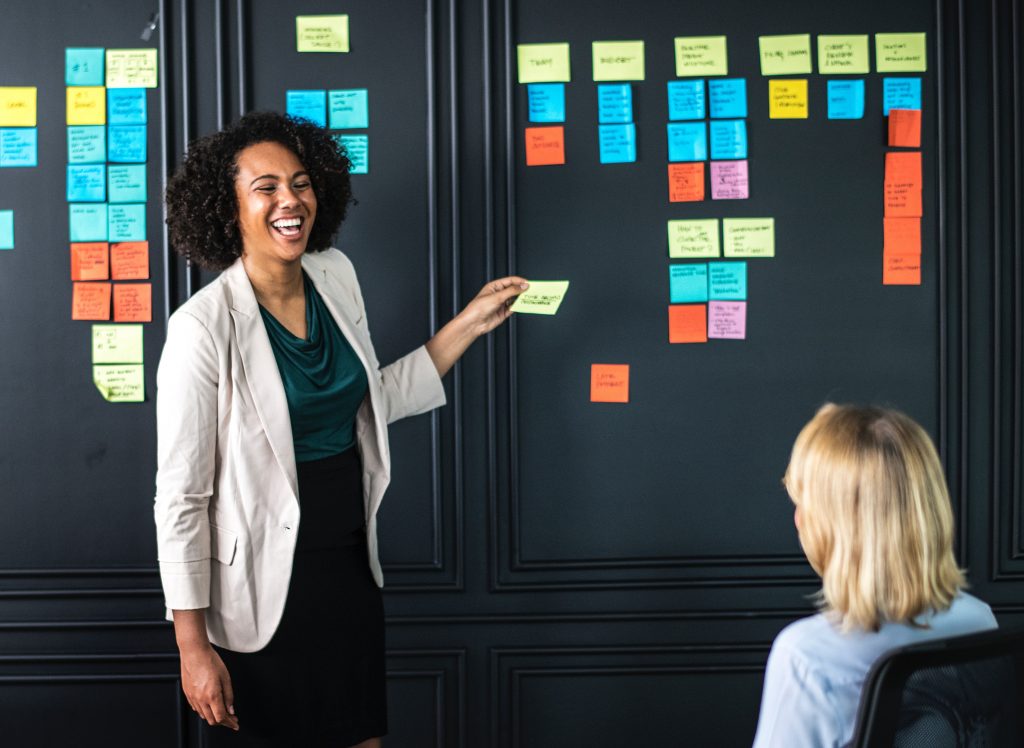 Woman of color with post-its smiling at blonde-haired woman