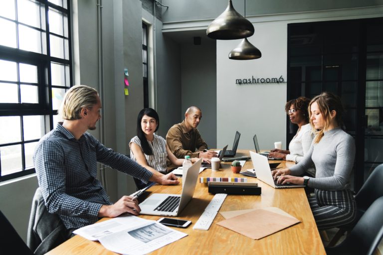 5 people at conference table with laptops