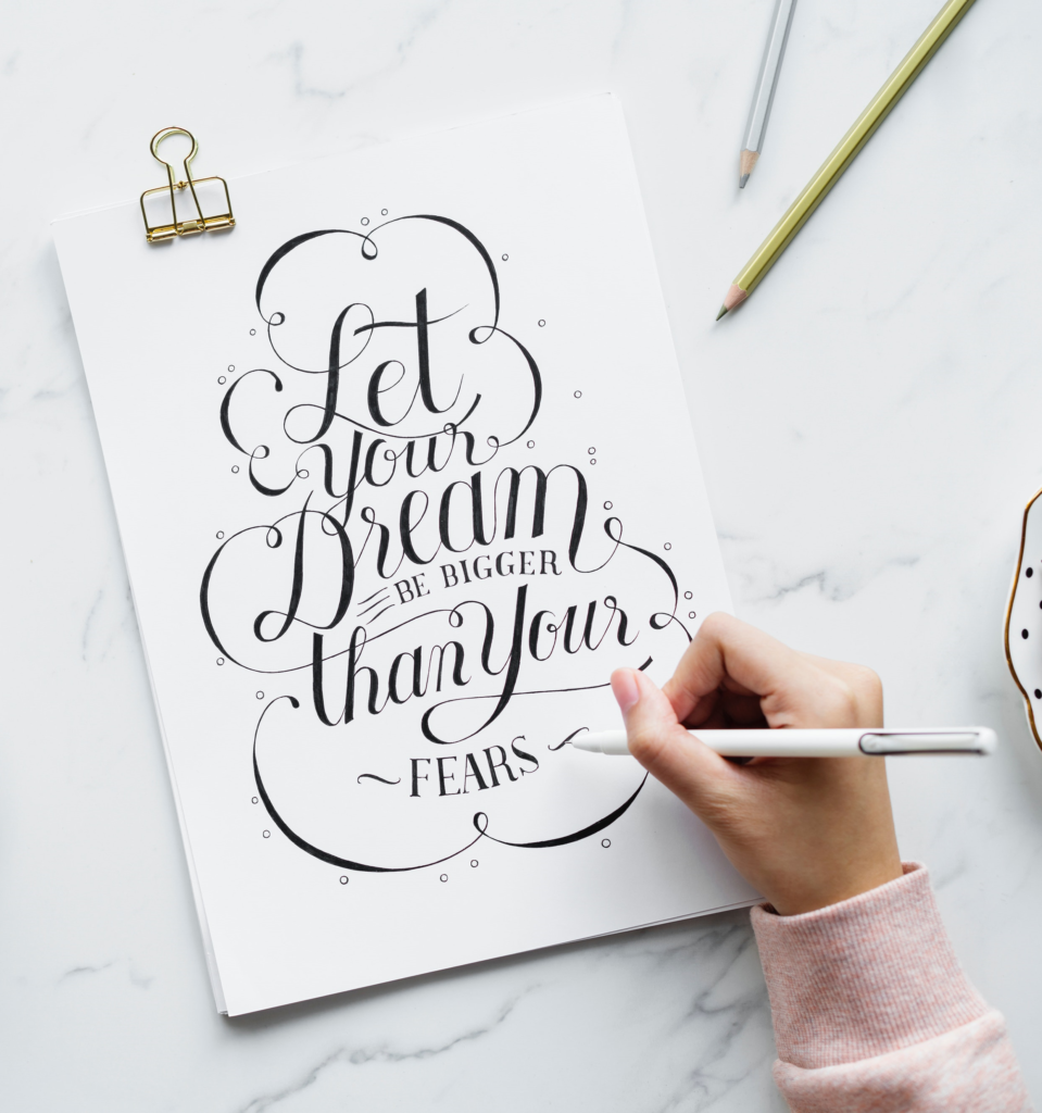 calligraphic text on a notepad reading "let your dreams be bigger than your fears"
